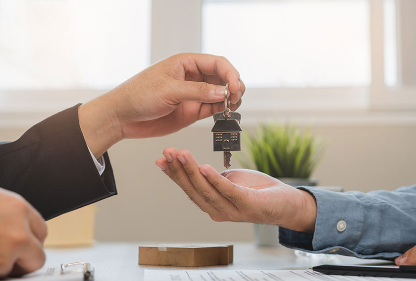 Real estate agent handing keys to a tenant after signing lease paperwork, representing Baltimore rental license compliance required before renting out a property.